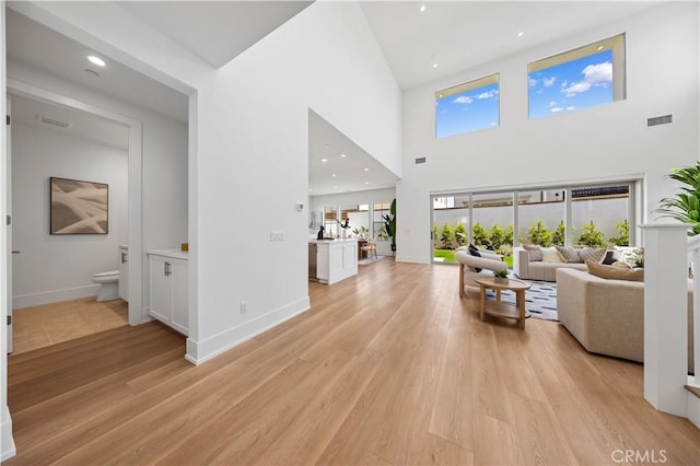 living area with baseboards, light wood finished floors, a towering ceiling, and visible vents