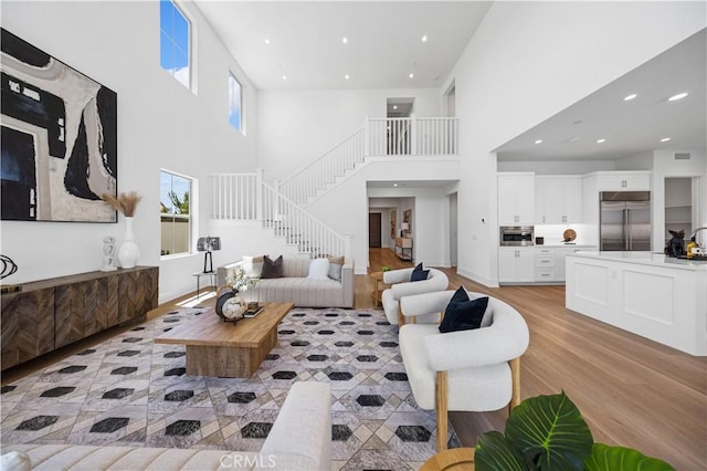 living room with recessed lighting, a high ceiling, stairs, and light wood-style flooring