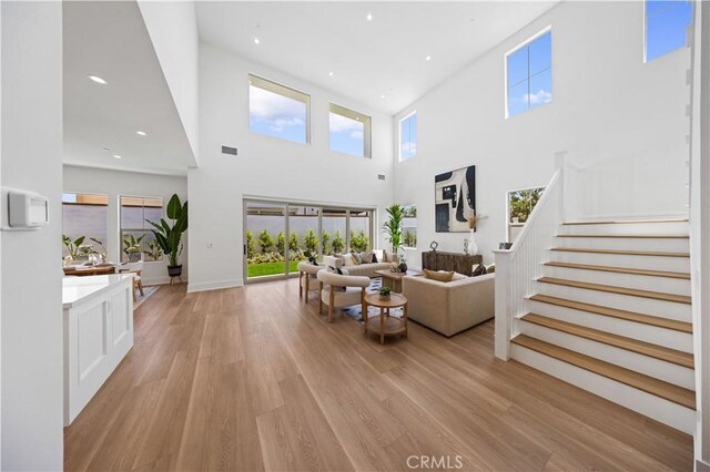 living area with a towering ceiling, light wood finished floors, and plenty of natural light