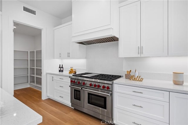 kitchen featuring light wood-type flooring, white cabinetry, light stone counters, and double oven range