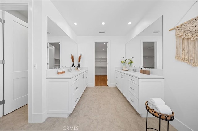 bathroom featuring tile patterned floors, two vanities, visible vents, recessed lighting, and a walk in closet