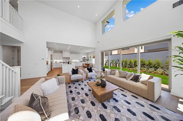 living room with baseboards, light wood finished floors, a towering ceiling, and visible vents