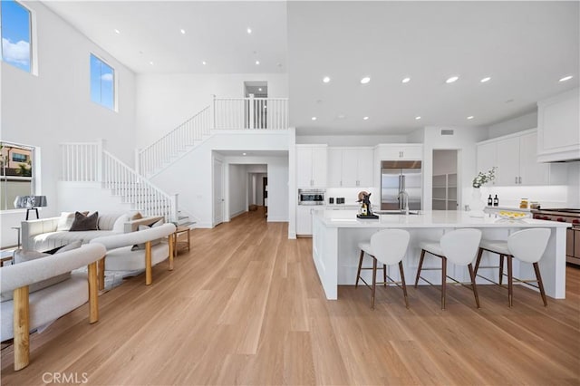 kitchen featuring premium appliances, a breakfast bar area, light wood finished floors, light countertops, and white cabinetry
