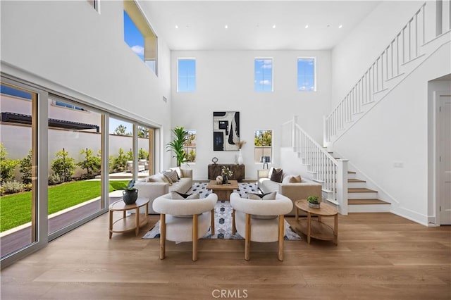 living area with recessed lighting, a towering ceiling, stairs, and light wood-style floors