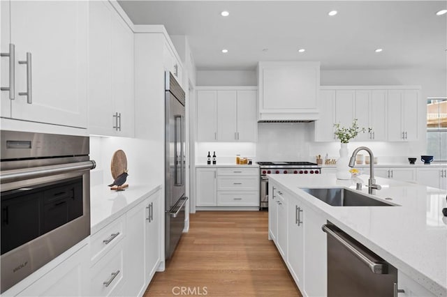 kitchen featuring white cabinets, custom exhaust hood, premium appliances, and a sink