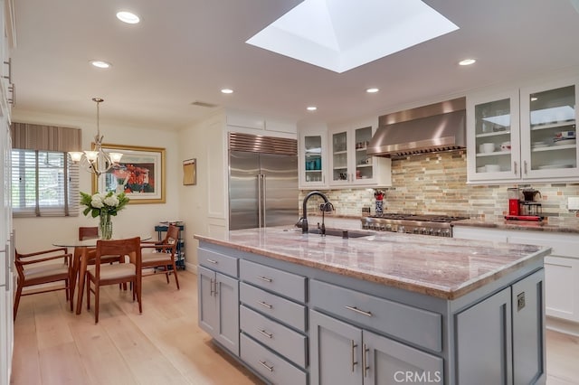 kitchen featuring wall chimney exhaust hood, gray cabinets, a sink, stainless steel appliances, and backsplash