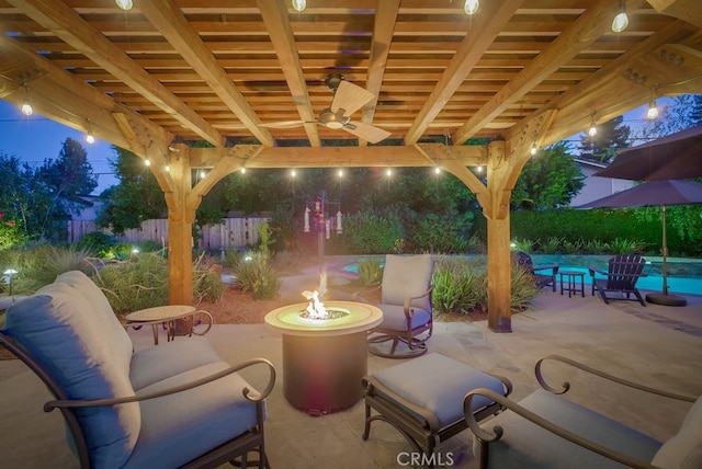 patio at night featuring a fenced in pool, a ceiling fan, fence, and an outdoor fire pit