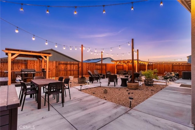 patio terrace at dusk featuring a fenced backyard, a fire pit, outdoor dining area, and cooling unit