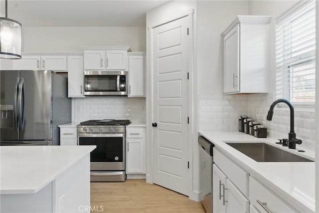 kitchen with appliances with stainless steel finishes, light countertops, white cabinets, decorative backsplash, and a sink