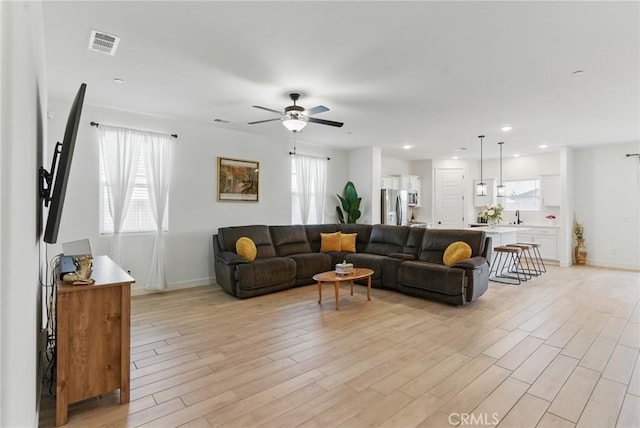 living room with light wood-style flooring, visible vents, baseboards, and a ceiling fan