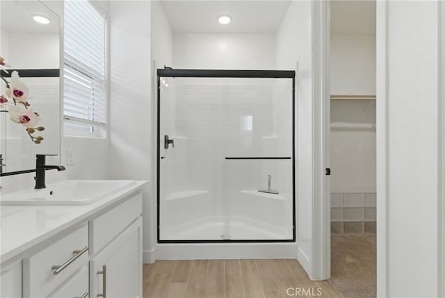 bathroom featuring a shower stall, wood finished floors, vanity, and a walk in closet