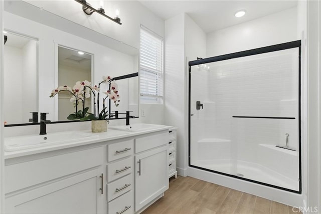 full bath with a sink, double vanity, a stall shower, and wood finished floors
