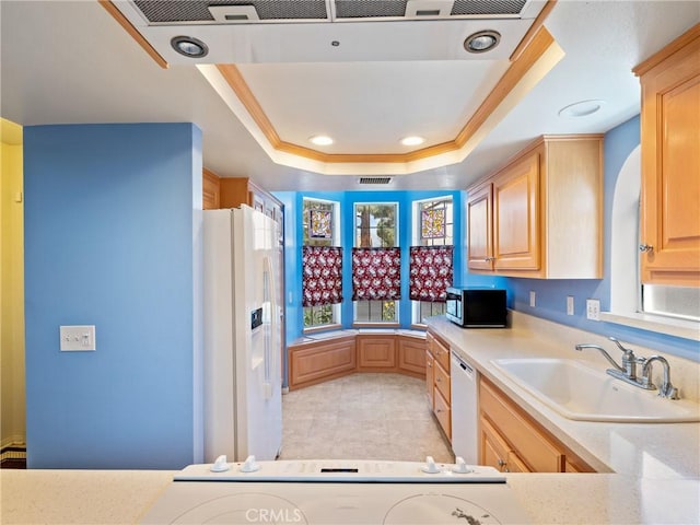 kitchen featuring light brown cabinets, a sink, white appliances, light countertops, and a raised ceiling