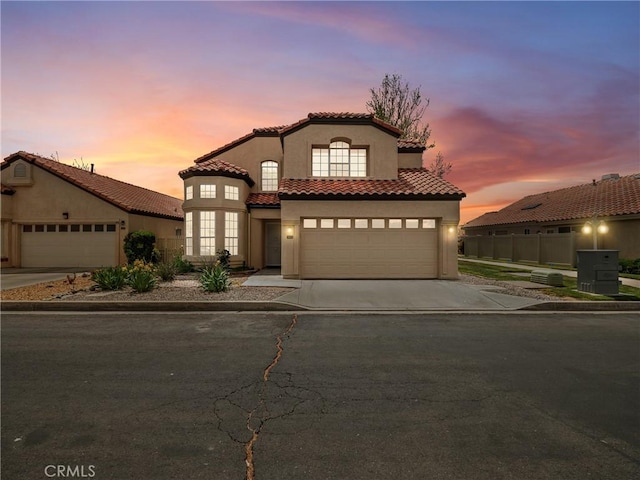 mediterranean / spanish-style house featuring stucco siding, a tile roof, driveway, and fence