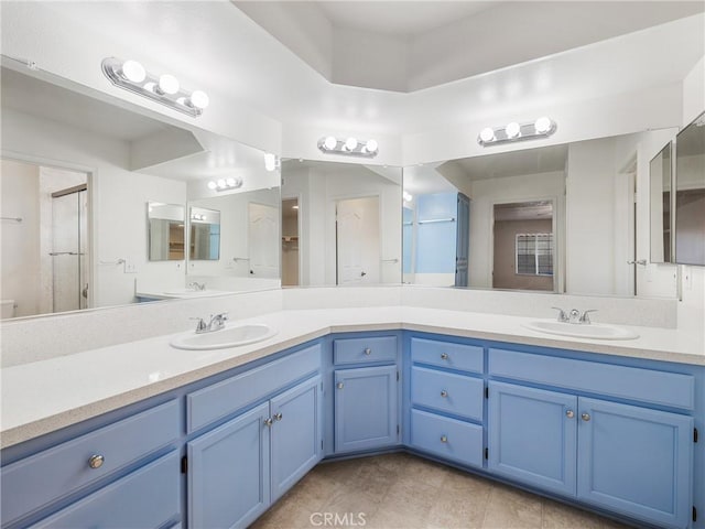 bathroom with a shower with shower door, a sink, and double vanity