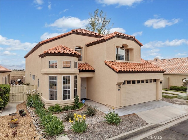 mediterranean / spanish-style home featuring driveway, a tiled roof, stucco siding, and fence