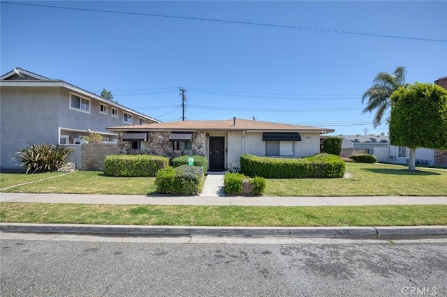 view of front facade featuring a front yard, stucco siding, and fence