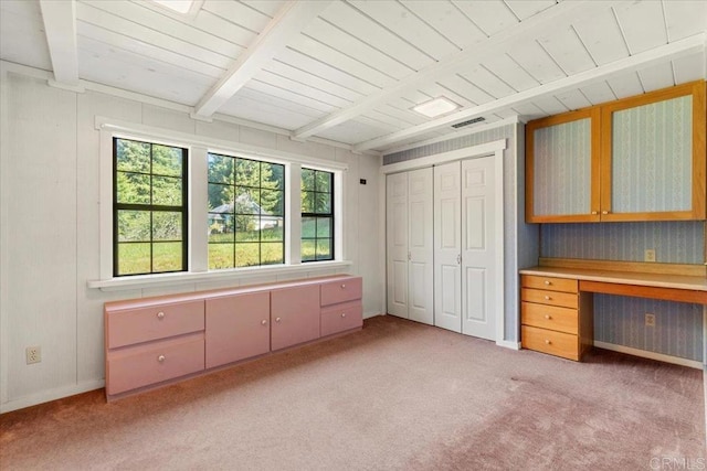 unfurnished bedroom featuring beamed ceiling, multiple windows, and light colored carpet