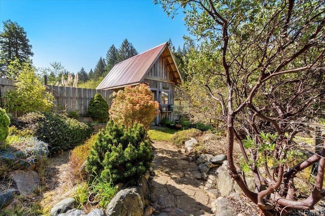 view of property exterior featuring metal roof, fence, and an outdoor structure