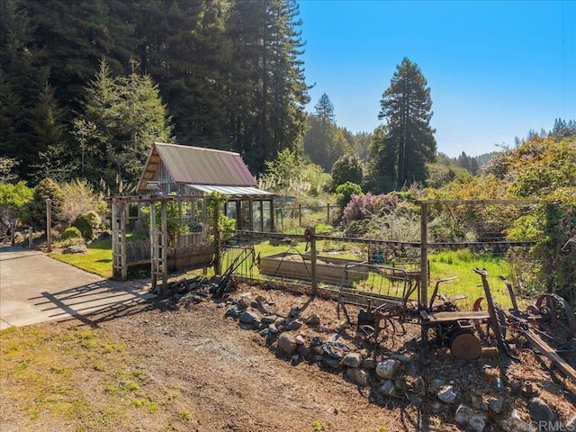 view of yard featuring an outbuilding, an exterior structure, a garden, fence, and a wooded view
