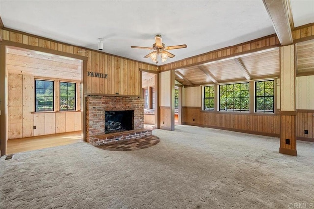 unfurnished living room featuring wood walls, plenty of natural light, visible vents, and a ceiling fan