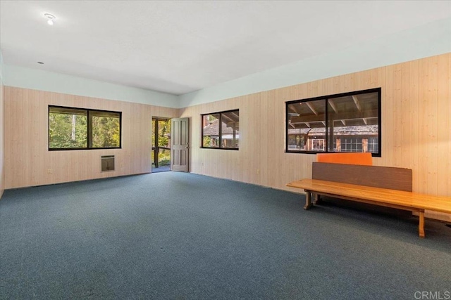 carpeted spare room featuring wood walls and heating unit