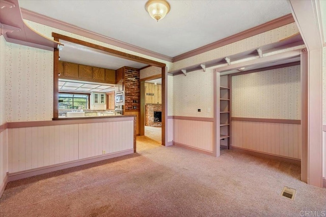 unfurnished living room featuring visible vents, a fireplace, carpet floors, wainscoting, and wallpapered walls