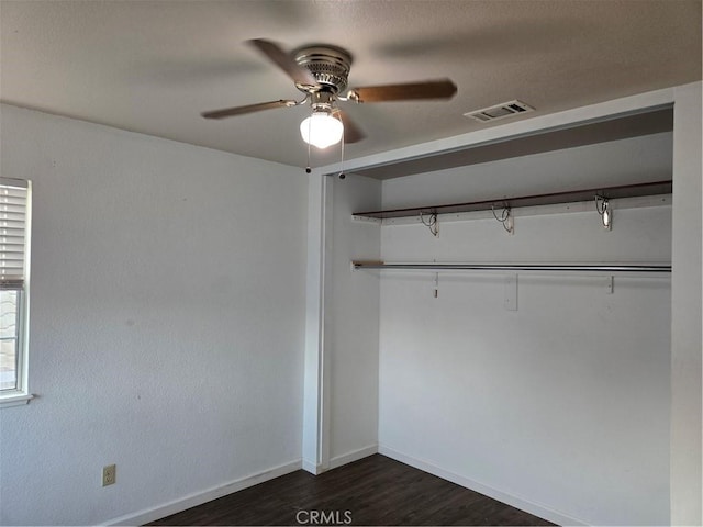 unfurnished bedroom with dark wood finished floors, visible vents, a ceiling fan, a closet, and baseboards