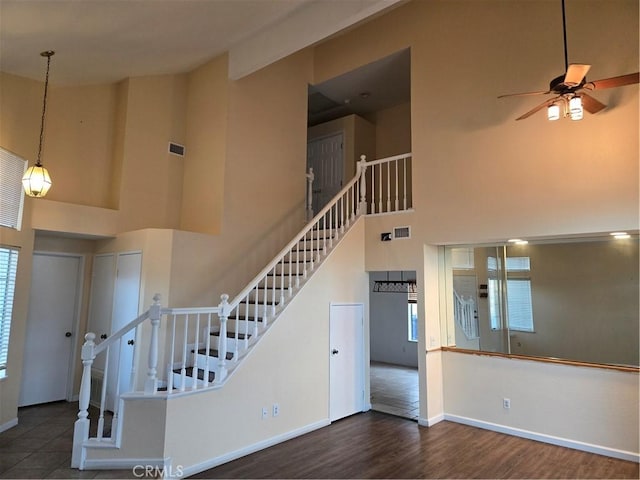 stairs featuring a ceiling fan, wood finished floors, a wealth of natural light, a towering ceiling, and visible vents