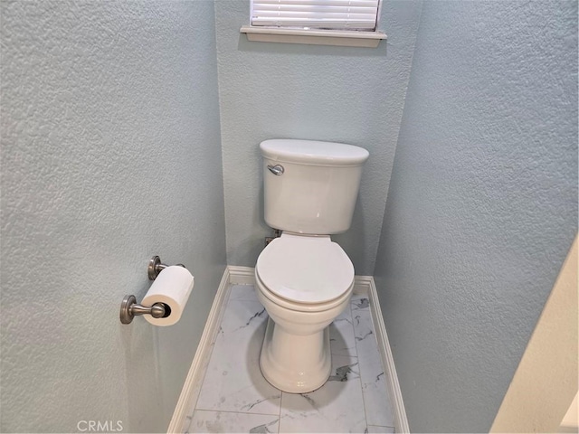 bathroom with marble finish floor, toilet, a textured wall, and baseboards