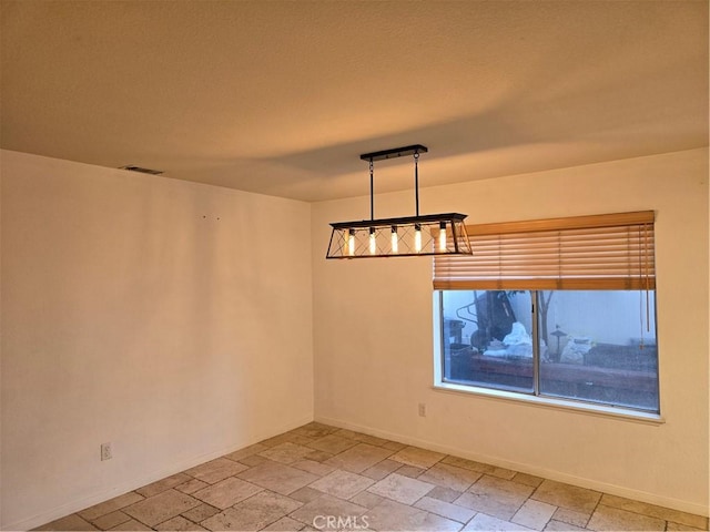 spare room featuring baseboards, stone tile flooring, and visible vents
