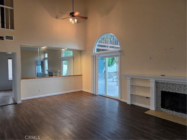 unfurnished living room with a fireplace with flush hearth, a towering ceiling, wood finished floors, and ceiling fan