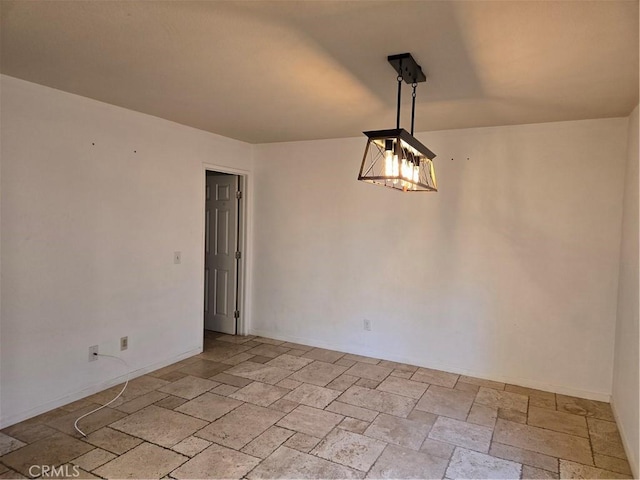 spare room featuring a chandelier, stone tile flooring, and baseboards