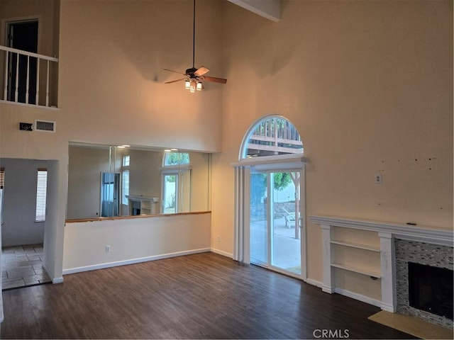 unfurnished living room with a fireplace with flush hearth, a towering ceiling, a ceiling fan, and wood finished floors