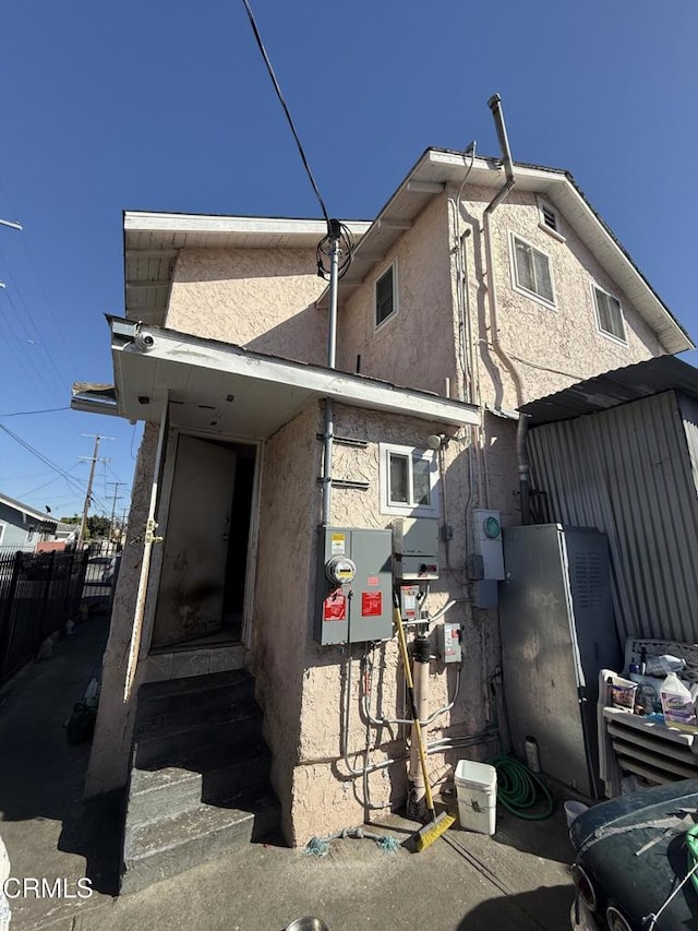 view of side of property featuring fence, stucco siding, and entry steps