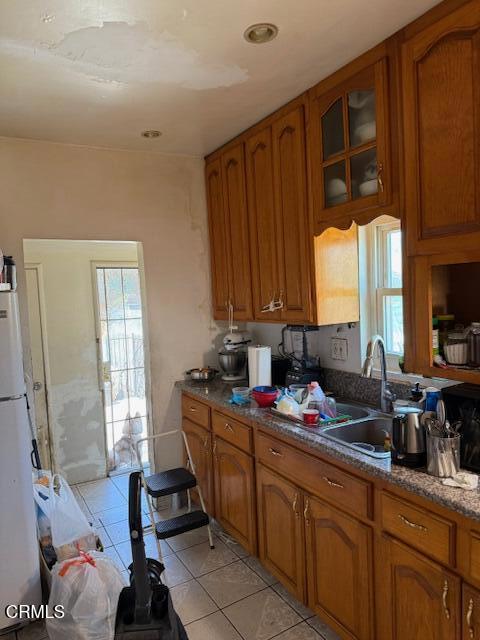 kitchen featuring plenty of natural light, brown cabinets, light tile patterned floors, a sink, and freestanding refrigerator