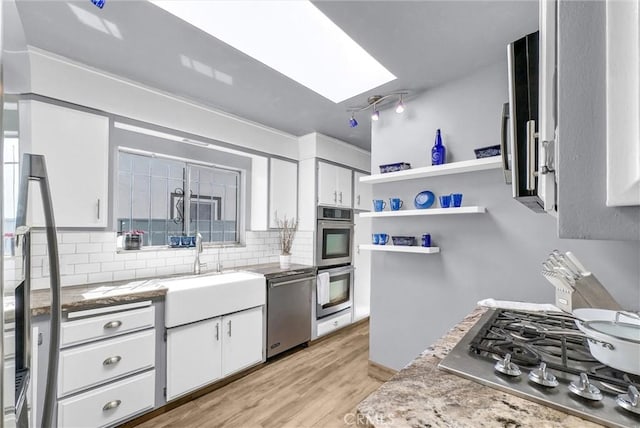 kitchen with tasteful backsplash, white cabinetry, a skylight, appliances with stainless steel finishes, and light wood finished floors