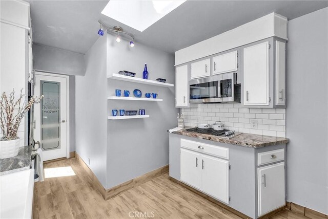 kitchen with a skylight, light wood-style floors, decorative backsplash, and stainless steel appliances
