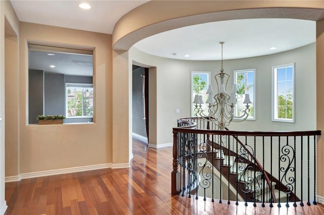 hallway with baseboards, wood finished floors, a chandelier, and plenty of natural light
