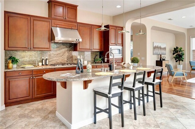 kitchen featuring backsplash, a breakfast bar area, under cabinet range hood, and stainless steel appliances