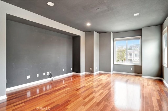 spare room with baseboards, wood finished floors, and recessed lighting