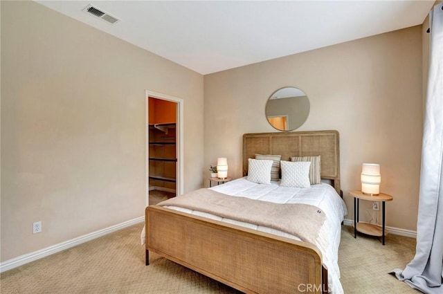 bedroom featuring a walk in closet, baseboards, visible vents, and light colored carpet