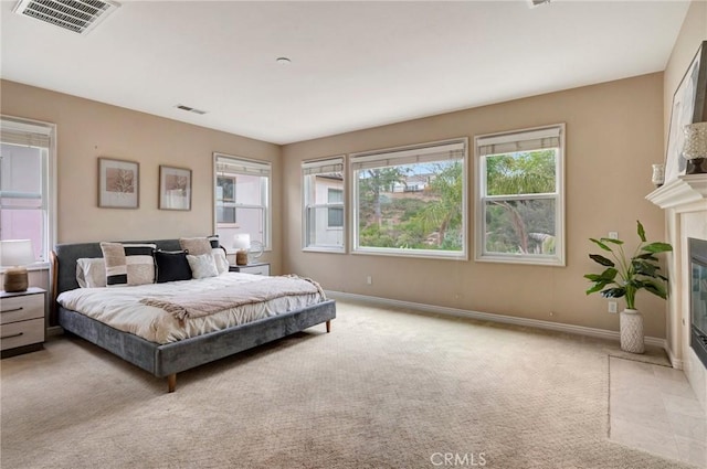 bedroom with a tiled fireplace, visible vents, baseboards, and light carpet