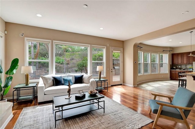 living area featuring arched walkways, light wood-style floors, and baseboards