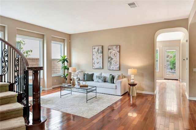 living room with arched walkways, wood finished floors, visible vents, and a wealth of natural light