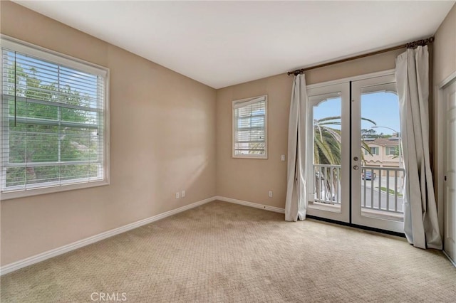 empty room with a wealth of natural light, french doors, and light carpet