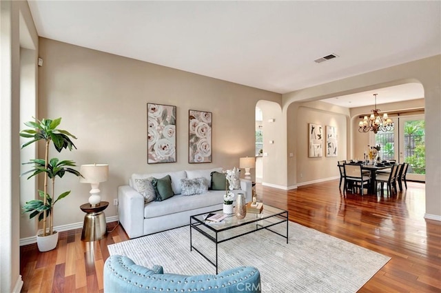 living room featuring wood finished floors, visible vents, arched walkways, baseboards, and a notable chandelier