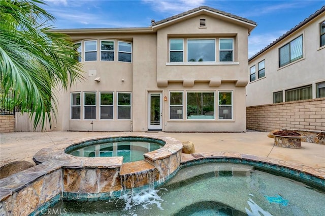 back of house featuring stucco siding, a patio, a fire pit, and an in ground hot tub