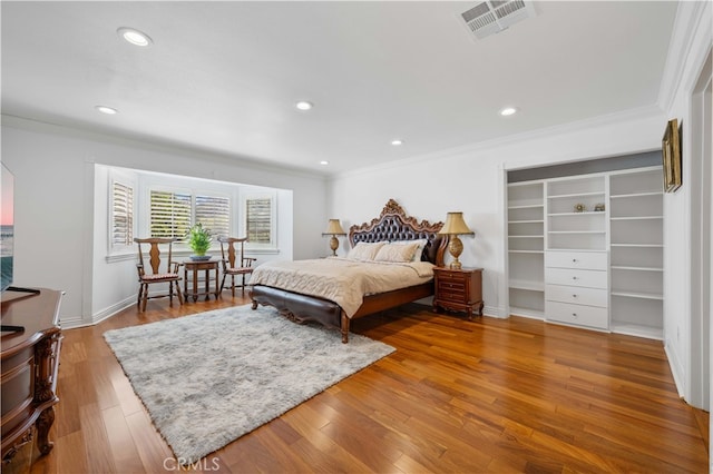 bedroom with crown molding, recessed lighting, wood finished floors, a walk in closet, and baseboards