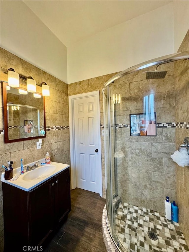 full bath featuring tile walls, a shower stall, vanity, and wood finished floors